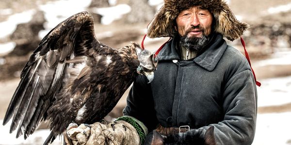 A man in traditional winter clothing holding a large eagle.