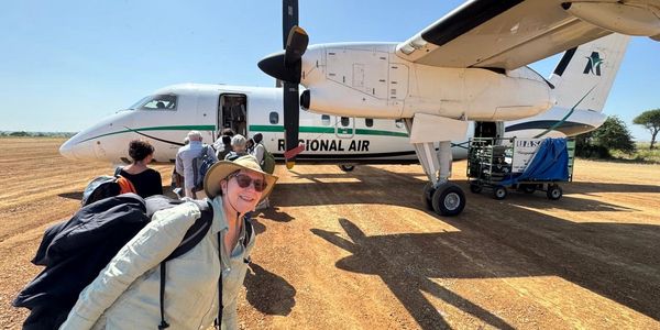 Smiling traveler with backpack boarding a Regional Air plane on a dirt runway.