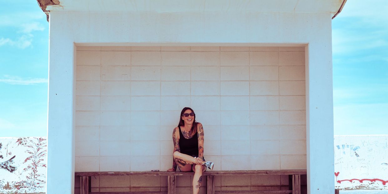 Tattooed woman in sunglasses sitting on a bench under a white shelter.
