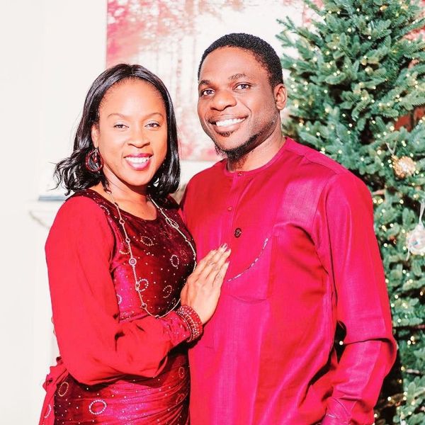 Couple dressed in matching red outfits smiling by a decorated Christmas tree.