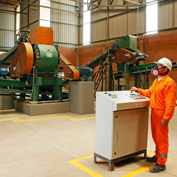 Worker in orange safety gear operating machinery in an industrial facility.