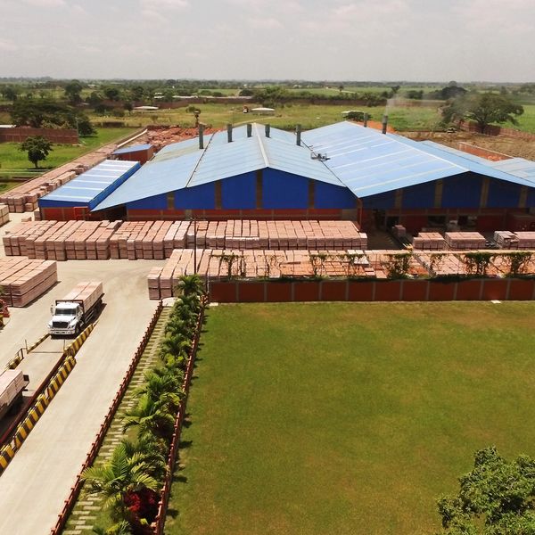 A large industrial facility with blue roofs and stacked bricks outside.