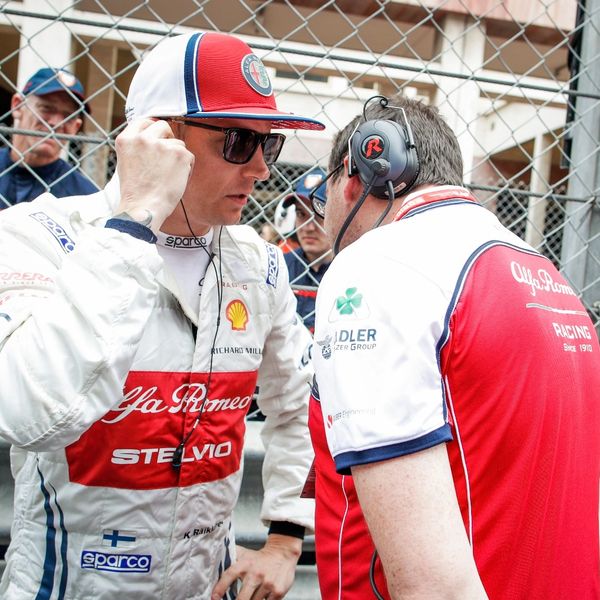 Alfa Romeo racing driver talks with a team member wearing headset before a race.