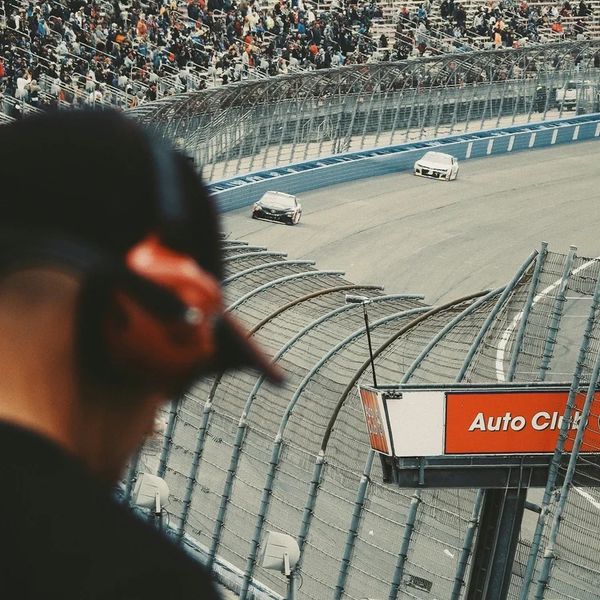 A man watches a car race from the stands at a crowded racetrack.