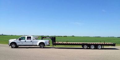 White pickup truck towing a flatbed trailer on a road.