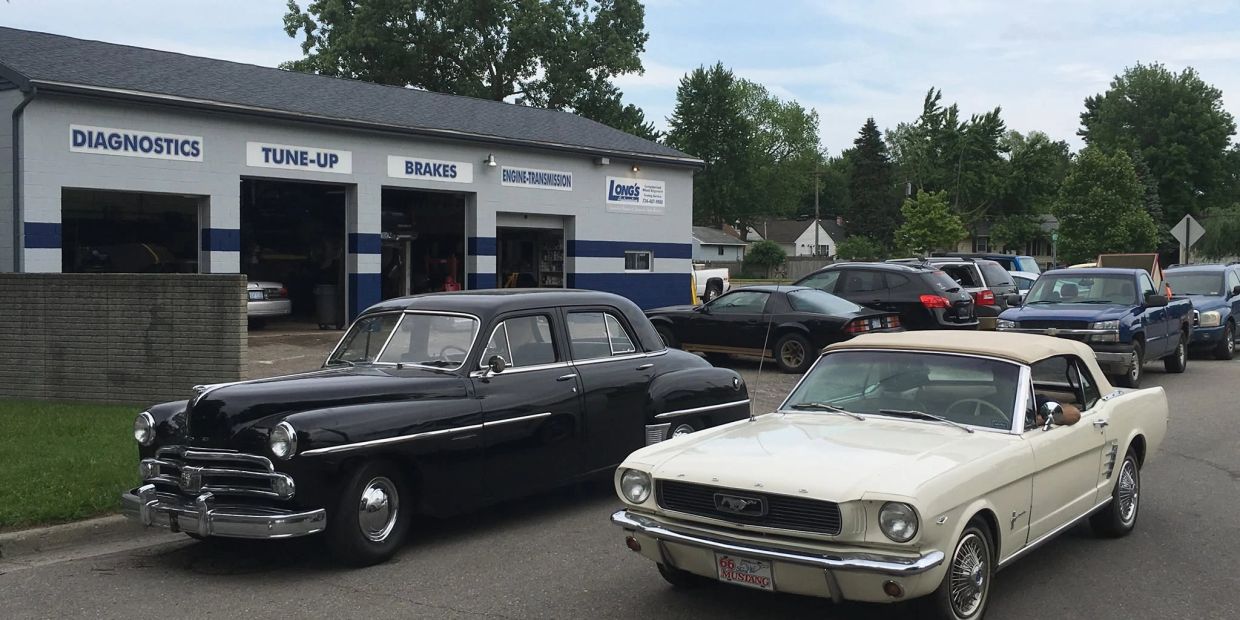 Two classic cars parked outside an auto repair shop.