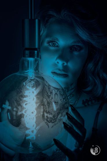 Woman illuminated by a glowing light bulb in dark setting.