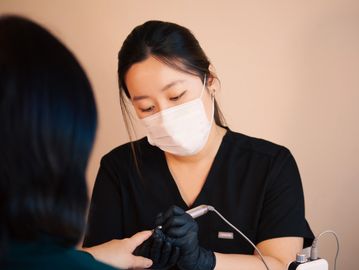 A masked nail technician carefully works on a client's nails.