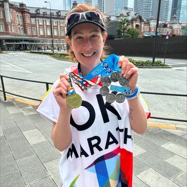 Smiling marathon runner holding Tokyo Marathon 2023 medals in an urban setting.