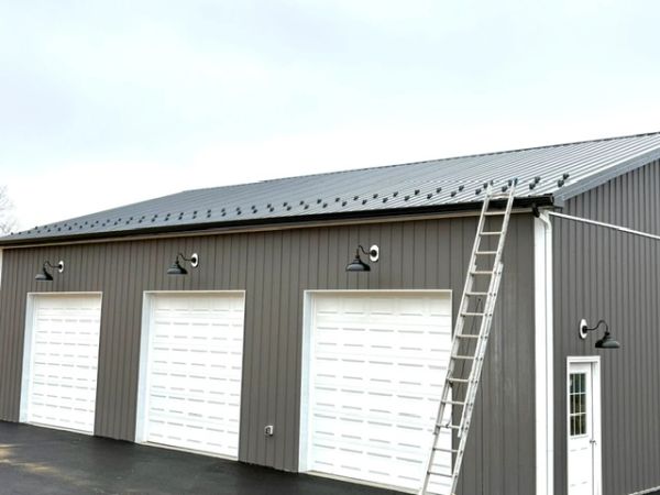 A gray building with three white garage doors and a ladder on the side.