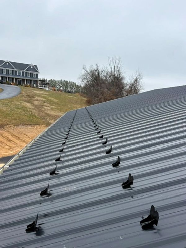 Close-up of a metal roof with mounting brackets in a rural area.