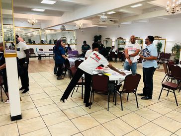 People gather at a community event with voter registration booths in a spacious hall.