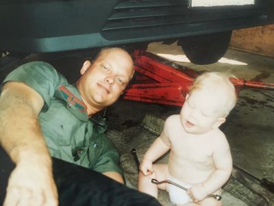 Man and baby under a car in a garage.