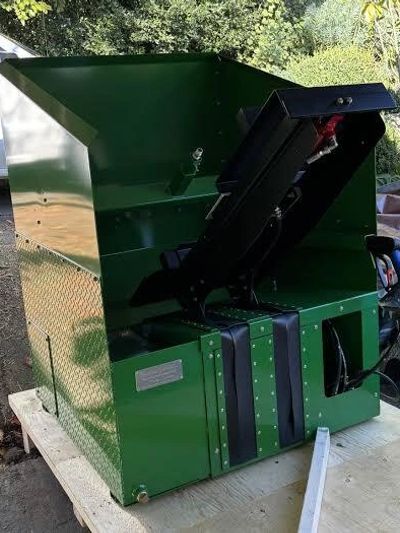 Large green metal machine with chute on wooden table outdoors.