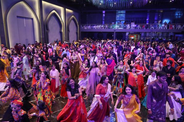 Large crowd dancing in colorful traditional dresses at a festive event.