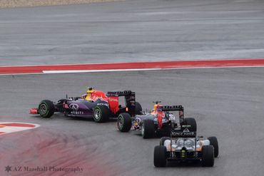 Three Formula 1 cars racing on a track during a turn.