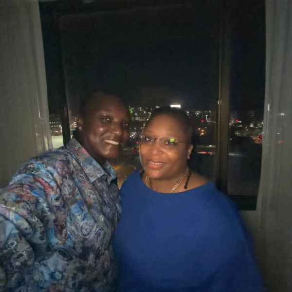 Two people smiling for a selfie at night with city lights in the background.