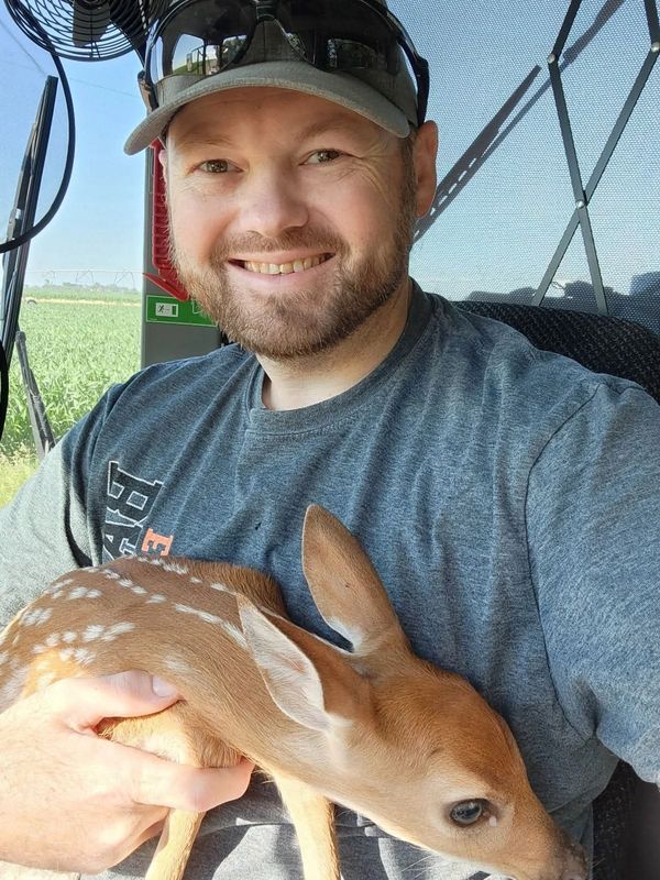 Man holding a young fawn and smiling.