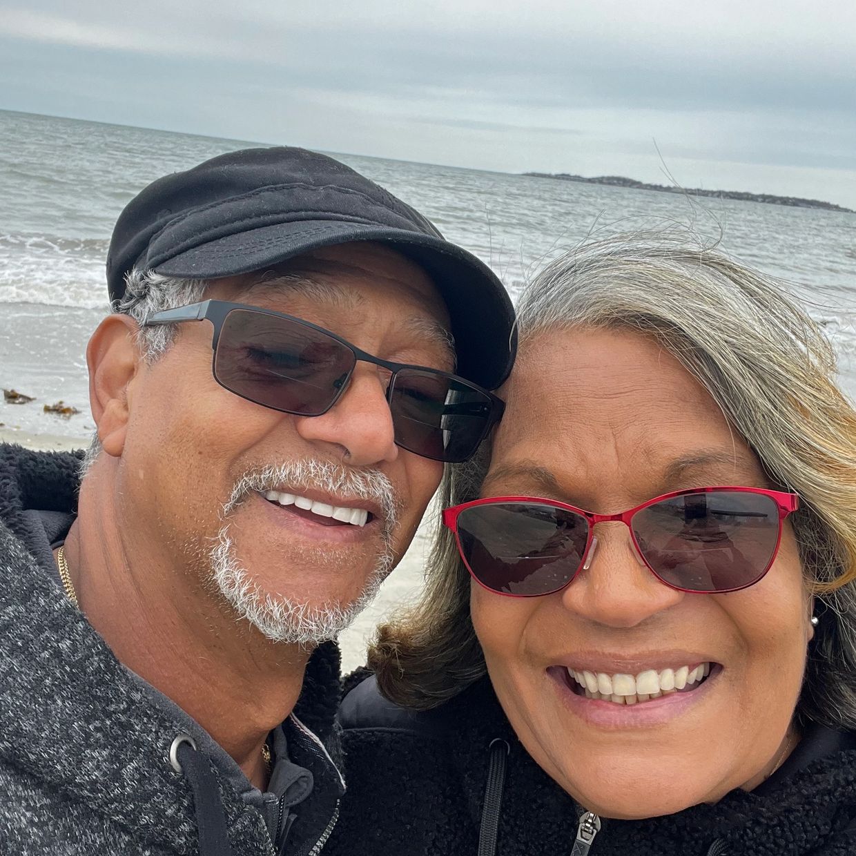 Smiling couple wearing sunglasses at the beach.