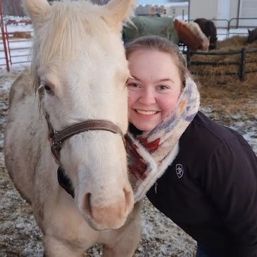A smiling woman hugs a white horse outdoors in winter.