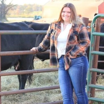 Young woman in plaid shirt stands by cattle gate on farm.