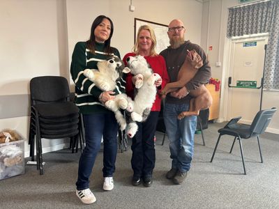 Group holding stuffed animals and dog indoors