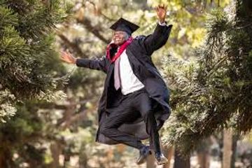 Excited graduate joyfully jumps outdoors in cap and gown.
