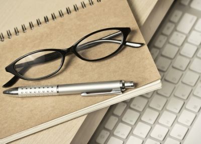 Eyeglasses and pen resting on a notebook above a keyboard.