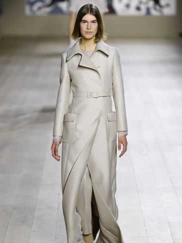 Model walks runway in a long beige coat.