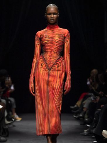 Model walks runway in vibrant orange and black striped dress.