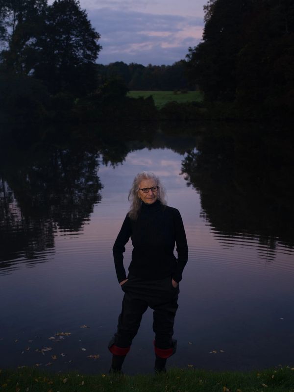 Woman standing near a calm lake at dusk.