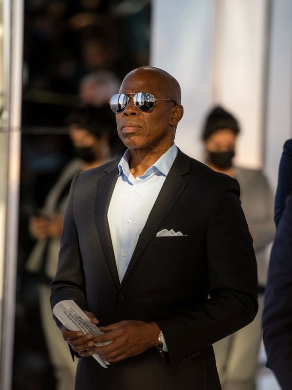 Man in a black suit wearing sunglasses and holding papers.