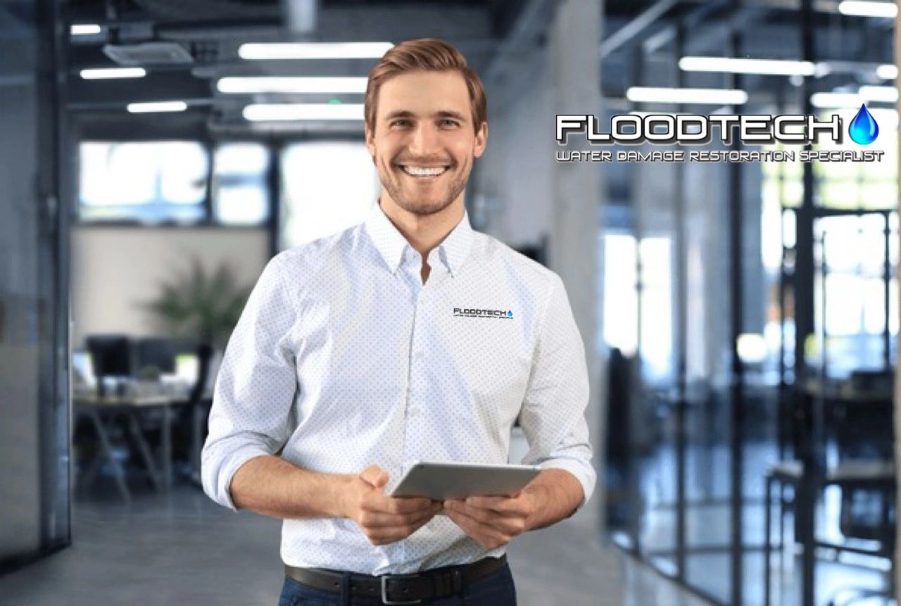Smiling man in office shirt holding a tablet with Floodtech logo.