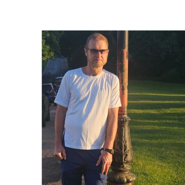 Man in sunglasses leans against a weathered lamp post in a sunny park. Birmingham Hip Replacement Personal Training | Always In Your Corner