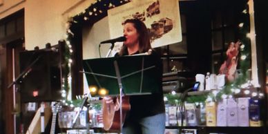 Woman singing and playing guitar on a decorated stage indoors.