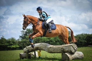 A rider on a horse jumping over a wooden obstacle in an outdoor setting.