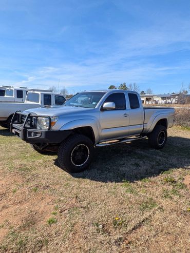 Silver lifted pickup truck parked on grass under a clear blue sky.