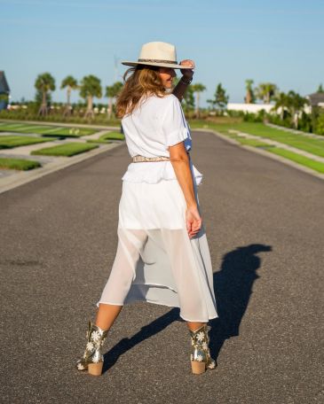 Woman in white outfit and hat posing on a sunny road.