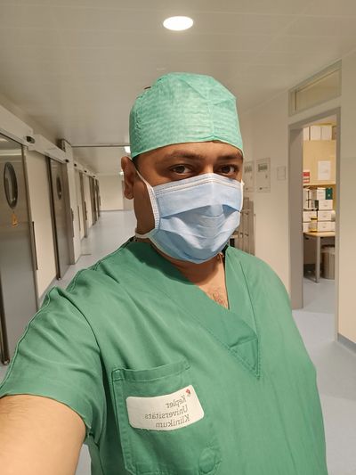Healthcare worker in green scrubs and mask in a hospital corridor.