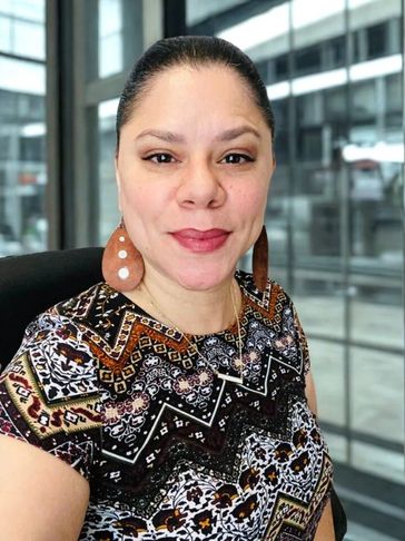 Smiling woman with patterned top and large earrings indoors.