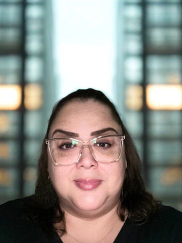 Smiling woman with glasses in front of a blurred window background.