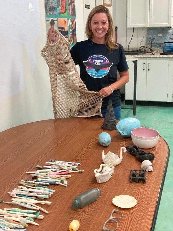 Woman showing various plastic objects collected on a table.