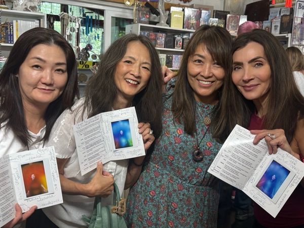 Four women smiling and holding up colorful printed papers in a bookstore.