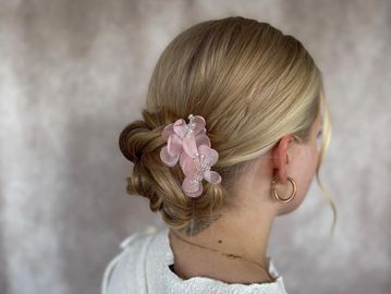 Elegant low bun hairstyle with a pink floral hair clip.