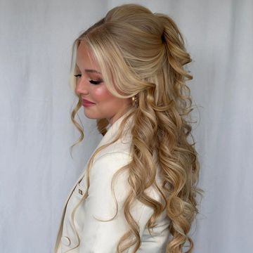 Woman with long, curly blonde hair styled elegantly in a white outfit.