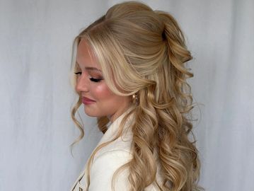 Elegant woman with long, curly blonde hair styled half-up, half-down.