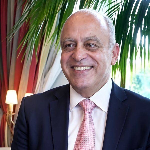 A smiling bald man in a suit and pink tie indoors with plants and lamps.