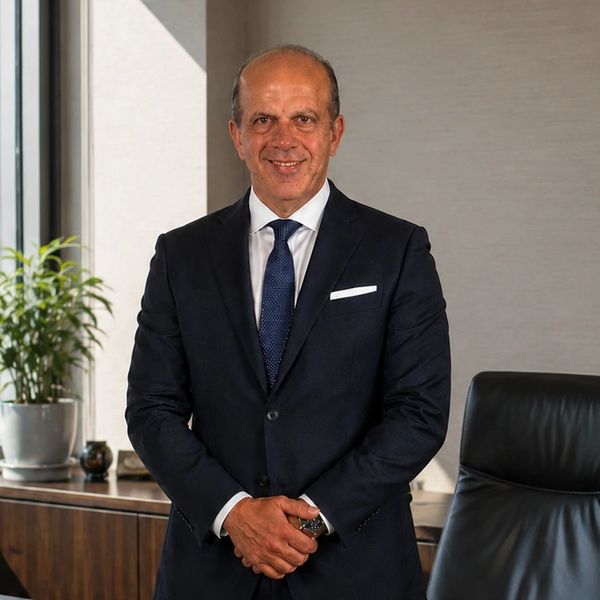 Confident man in a suit standing in a modern office with plants and leather chair.