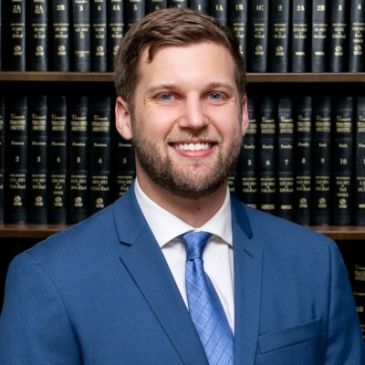 Man in blue suit smiling in front of law books.