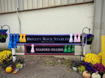 Award ribbons displayed on a Breezy Rock Stables sign with flowers and pumpkins.
